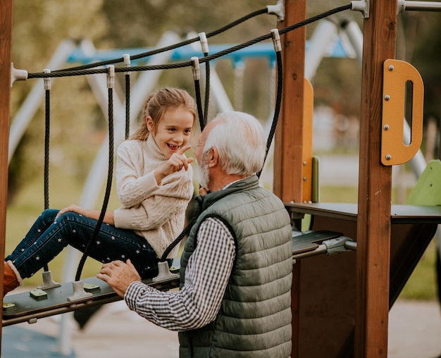 Grand-père passe du temps avec sa petite-fille dans l'aire de jeux du parc le jour de l'automne