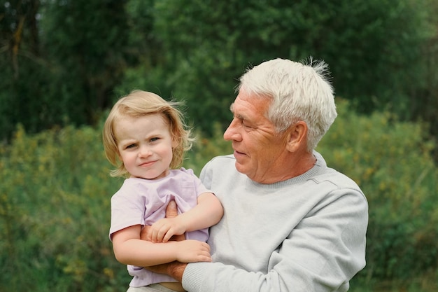 Grand-père et petit-enfant bébé s'amusent pendant la promenade dans le parc Famille heureuse Vieil homme grand-père étreignant une fille de 2 ans le jour d'été Souriant Senior homme passant du temps avec sa petite-fille ensemble