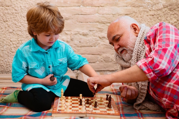 Grand-père et petit-fils jouent aux échecs et souriant tout en passant du temps ensemble à la maison mature m