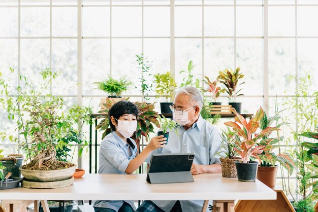 Photo grand-père et petit-fils de retraite asiatique portant un masque facial et vivent pour vendre des plantes sur une tablette avec plaisir.