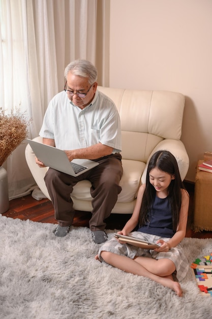 Grand-père et petite-fille apprennent en ligne à la maison. Mode de vie à l'âge de la retraite en famille pendant les vacances d'été.