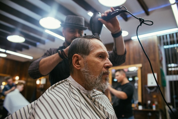 Grand-père se coupe les cheveux chez le coiffeur du salon de coiffure. Coupe de cheveux à la mode d'un vieil homme, un retraité dans le salon de coiffure. Soins des cheveux et de la barbe. ,