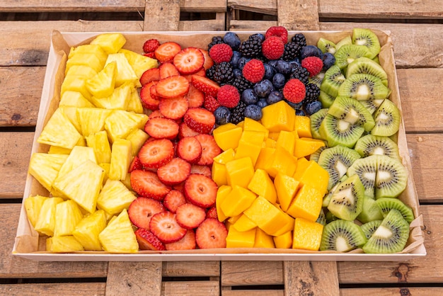 Grand plateau de fruits assortis hachés avec ananas mangue kiwi fraises et fruits rouges dans des boîtes de fruits