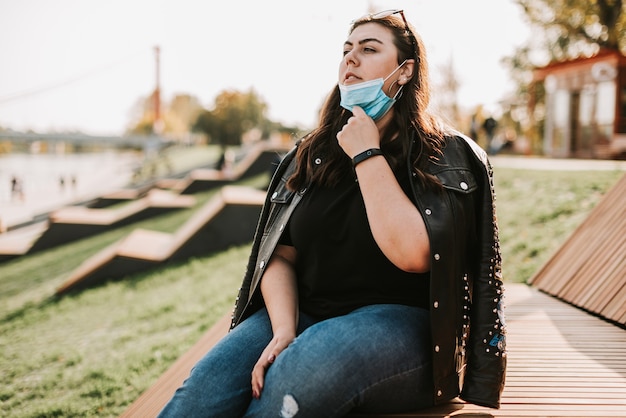 Grand portrait d'une belle femme dans un masque médical et une veste en cuir dans un parc dans la nature