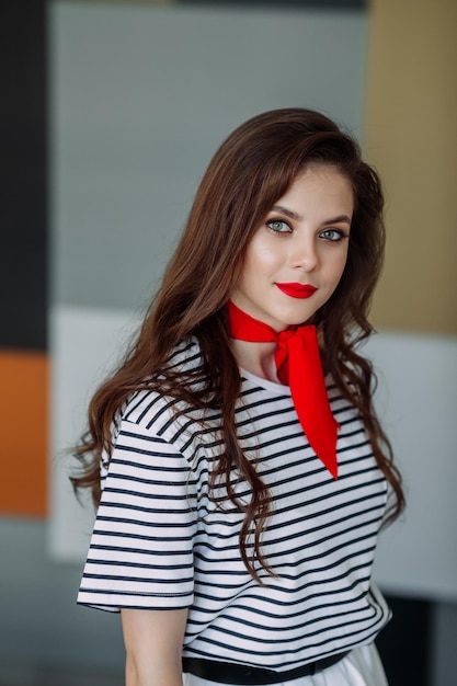 Un grand portrait d'une belle fille dans un chemisier rayé et une écharpe rouge autour