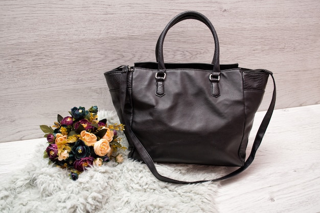 Grand sac femme noir sur bois, bouquet de fleurs et fourrure artificielle grise.