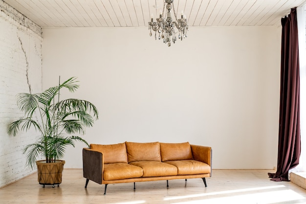 Un grand salon luxueux et lumineux avec une grande plante verte en pot dans un style industriel avec un canapé en cuir marron et un mur en brique et blanc.