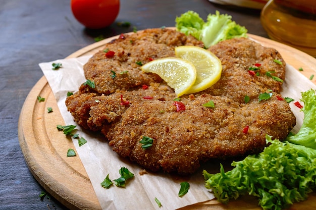 Grand schnitzel viennois sur une planche de bois avec du citron sur fond sombre. Plat de viande