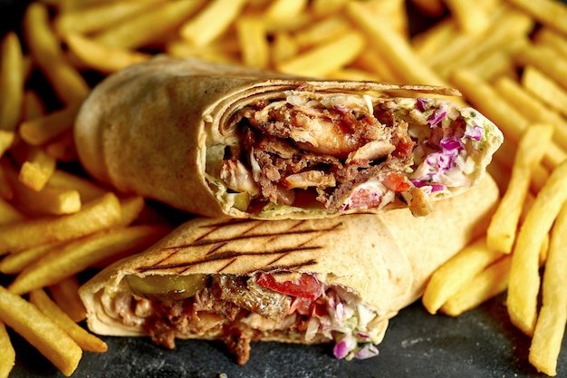 Photo grand shawarma avec légumes et viande sur fond sombre avec frites. gros plan, mise au point sélective