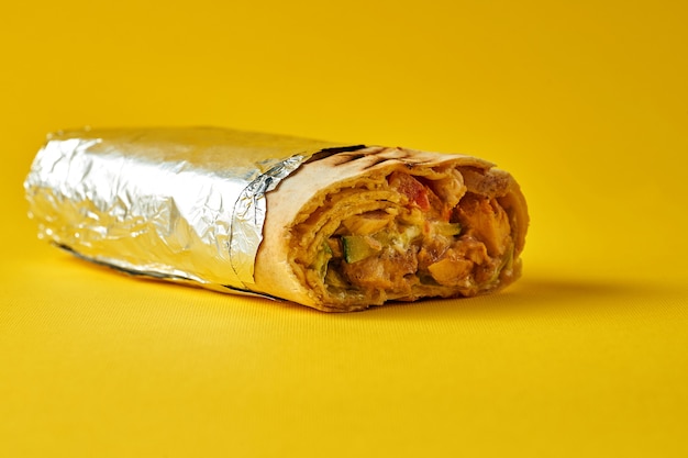 Grand shawarma avec viande et légumes, enveloppé dans du papier d'aluminium sur fond jaune. Gros plan, mise au point sélective