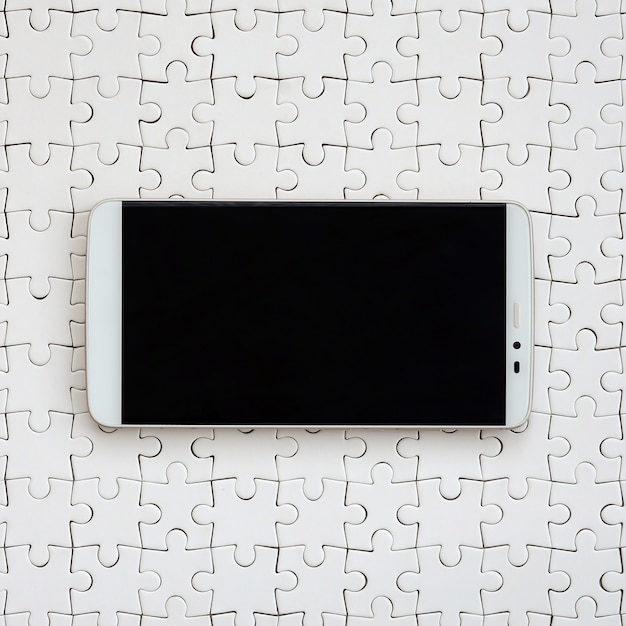 Un grand smartphone moderne doté d&#39;un écran tactile repose sur un puzzle blanc assemblé
