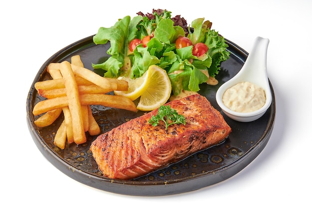 Un grand steak de saumon servi avec des frites frites, de la salade fraîche et des tomates.