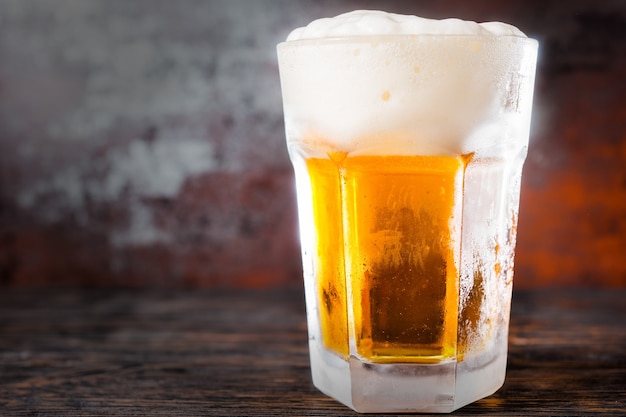 Grand verre avec une bière légère et une grosse tête de mousse sur un vieux bureau sombre. Concept de boissons et de boissons