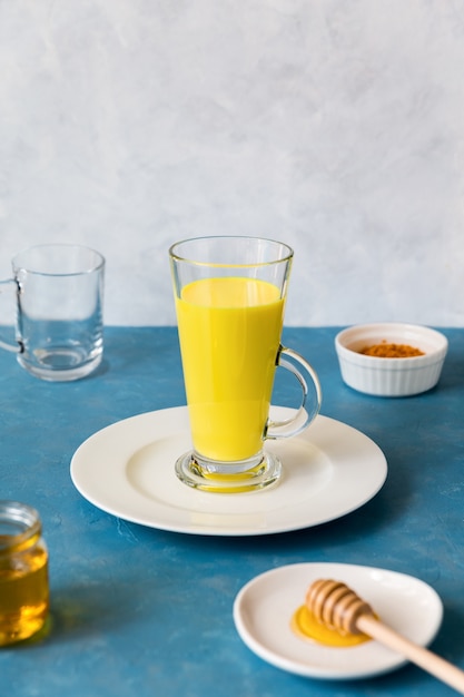 Grand verre avec une boisson au curcuma aux herbes lait doré se dresse sur une assiette blanche.