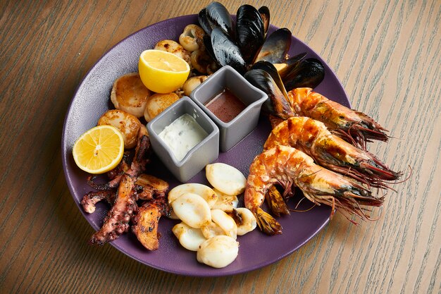 Une grande assiette de fruits de mer frits - calamars, poulpes, moules, pétoncles, crevettes. Assortiment de fruits de mer sur une plaque en céramique sur une surface en bois. Effet film pendant le post. Flou artistique