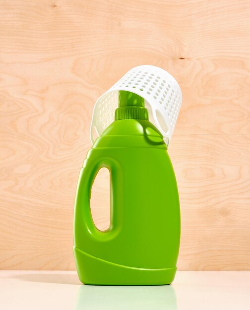 Grande bouteille verte de détergent liquide à lessive et panier à lessive blanc sur fond de bois