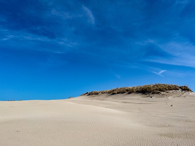 Une grande dune de sable avec un ciel bleu en arrière-plan.