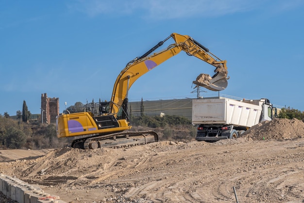 Grande excavatrice jaune déposant du sable dans un lit de camion sur un grand chantier de construction