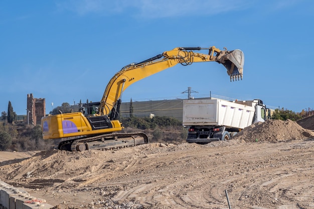 Grande excavatrice jaune déposant du sable dans un lit de camion sur un grand chantier de construction