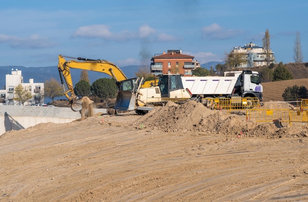 Grande excavatrice jaune déposant du sable et de la terre dans un lit de camion blanc sur un grand chantier de construction