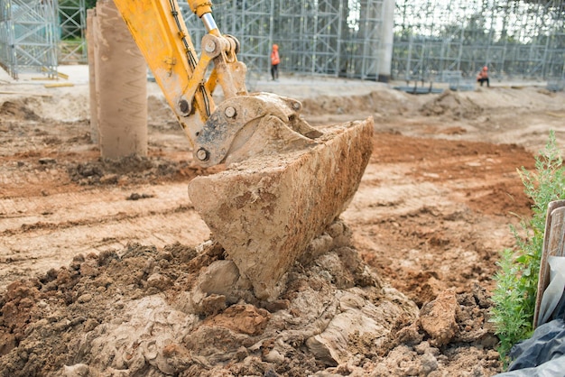 Une grande excavatrice jaune avec un godet avant recueille la terre sur un gros plan de chantier