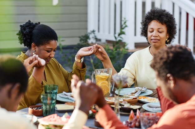 Grande Famille Afro-américaine Disant Grâce à Table à L'extérieur Et Se Tenant La Main Pendant Le Rassemblement
