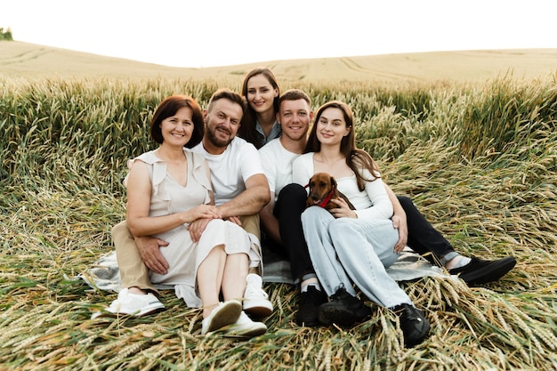 Une grande famille de cinq personnes est assise dans un champ de blé au coucher du soleil. câlins de famille heureux lors d'un pique-nique. vacances en famille pour parents avec enfants