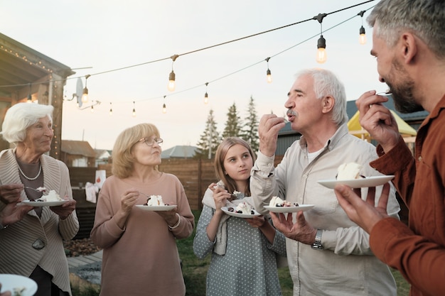 Grande famille debout dans le cercle et manger un gâteau ensemble pendant la fête à l'air frais