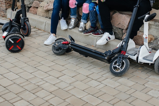 Une grande famille heureuse monte des Segways et des scooters électriques dans le parc par une chaude journée d'automne au coucher du soleil