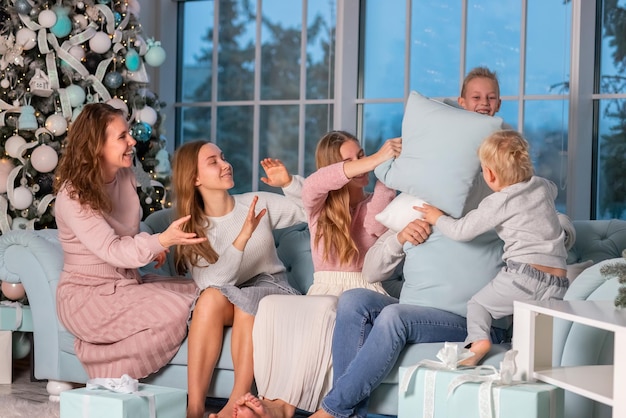 Grande famille heureuse avec de nombreux enfants ayant une bataille d'oreillers sous le sapin de Noël la veille de Noël