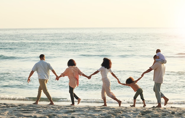 Grande famille marchant et se tenant la main à la plage au coucher du soleil s'amusant et se liant en vacances à l'extérieur Maquette de soins et enfants grand-mère et grand-père avec la mère et le père profitant des vacances