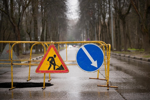 Grande fosse sur la route avec une clôture et des panneaux d'avertissement De fortes pluies ont emporté le sol Affaissement du sol Effondrement