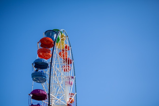 Une grande grande roue contre un ciel bleu. Des stands avec des gens montent. Il y a une place pour le texte. Concept : animations les vacances d'été, vacances avec enfants le week-end, balades en manèges.