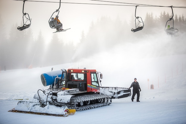 Grande machine de nettoyage de neige travaillant sur la pente de ski sous des chaises de câble