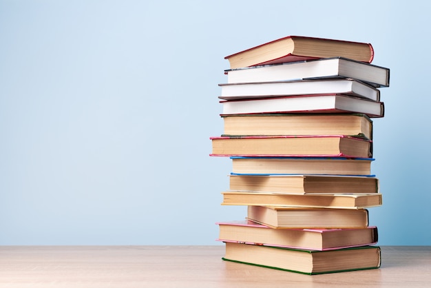 Une grande pile de livres chaotique se dresse sur une table en bois contre un mur bleu clair