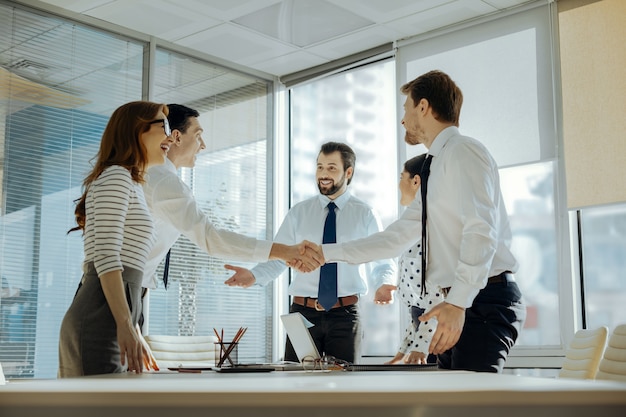 Grande réussite. De jeunes employés optimistes souriants et se serrant la main tout en se félicitant du succès du projet