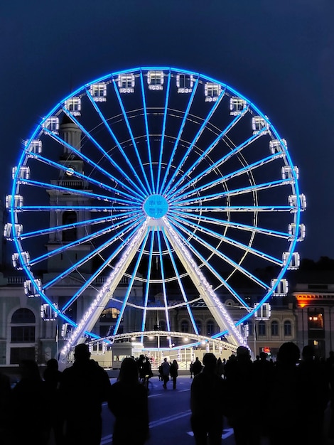 La grande roue sur la place de la ville est éclairée par des lumières électriques. Des personnes méconnaissables