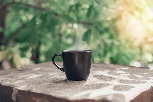 Grande tasse noire de thé noir avec de la vapeur blanche sur le bord du balcon en pierre dans la lumière du matin avec copie espace.