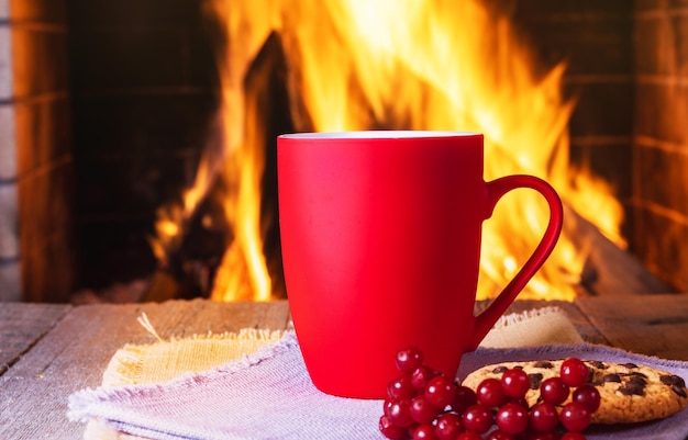 Grande tasse rouge de thé ou de café devant une cheminée confortable une cheminée confortable, dans une maison de campagne.