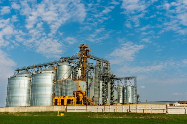 Une grande usine moderne pour le stockage et le traitement des cultures céréalières vue sur le grenier par une journée ensoleillée Grands barils de fer de silos d'argent à grains sur l'agro-usine pour le traitement et le séchage