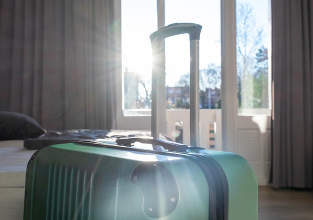 La grande valise verte reste dans la chambre de l'hôtel près de la fenêtre ou du balcon avec la lumière du soleil