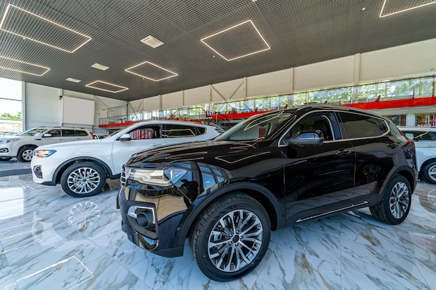 Une grande voiture de luxe sombre se trouve dans une salle d'exposition moderne. Vente de voitures dans le centre de concession. Beaucoup de voitures à vendre. Fermer.