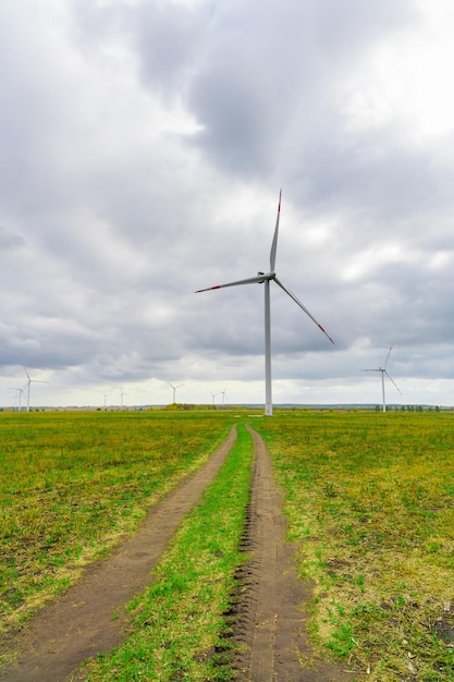 Grandes éoliennes avec pales dans le parc éolien sur fond de ciel nuageux. La route de campagne. Moulins à vent de silhouettes dans le champ. Énergie alternative.