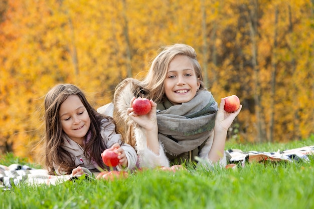 grandes et petites soeurs se trouvent, jouent avec des pommes rouges sur fond d'herbe verte d'arbres d'or de la forêt d'automne