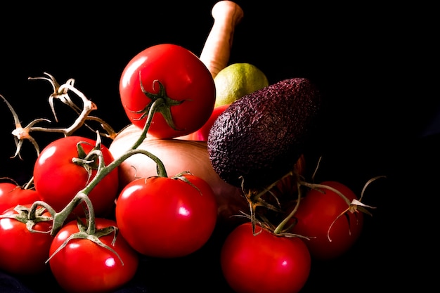 Grandes tomates rouges et mûres avec un mortier et un pilon en bois d&#39;olivier sur fond noir