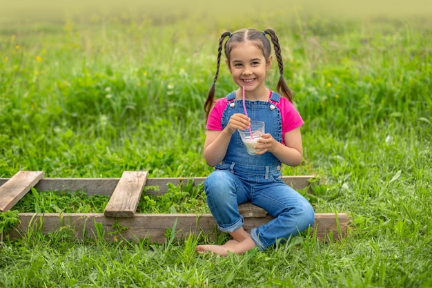 Grandhomme en salopette en jean et un T-shirt rose, tient un verre de lait sur une herbe verte