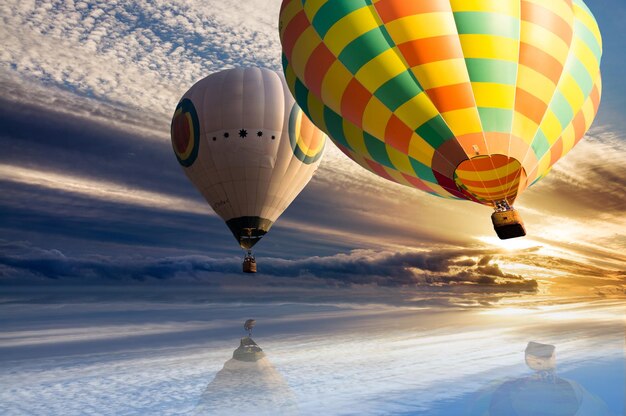 Grands ballons à air chaud colorés volant haut dans le ciel bleu nuageux pendant le coucher du soleil