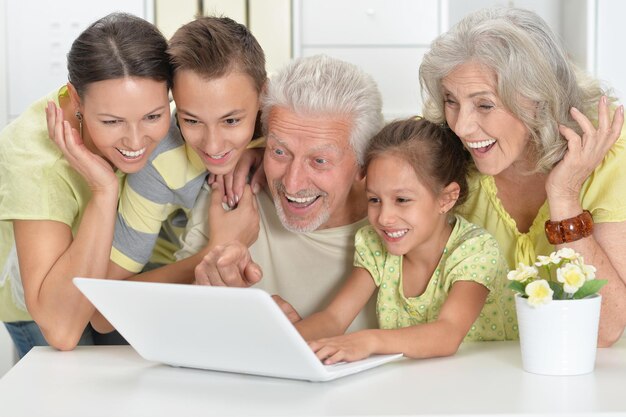 Photo grands-parents avec fille adulte et petits-enfants utilisant un ordinateur portable ensemble à la maison