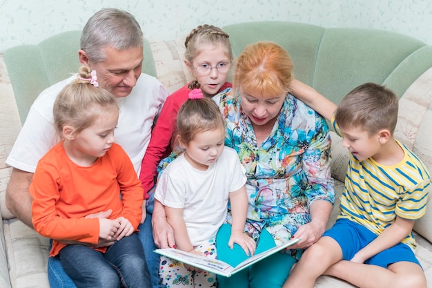 Grands-parents lisant un livre à leurs petits-enfants assis sur un canapé dans la chambre