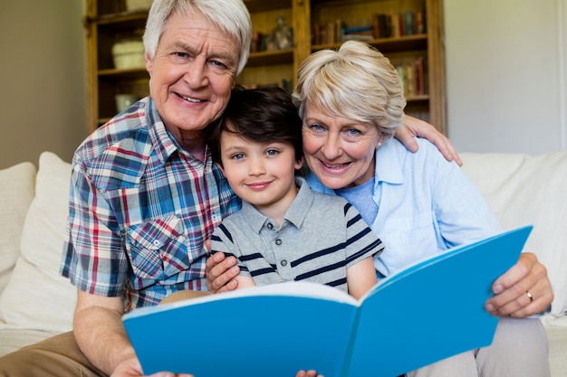 Grands-parents et petit-fils tenant un livre dans le salon